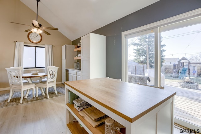 dining room with ceiling fan, baseboards, light wood-style floors, and vaulted ceiling