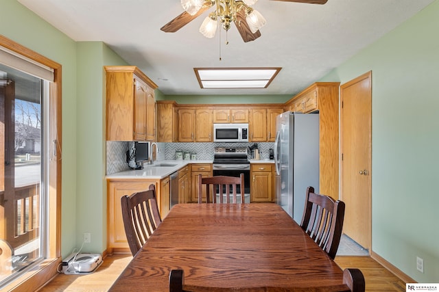 kitchen with a sink, stainless steel appliances, light countertops, decorative backsplash, and ceiling fan