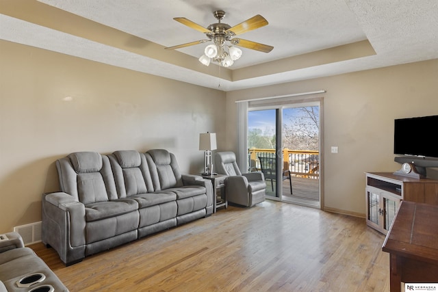 living room featuring light wood-type flooring, a tray ceiling, baseboards, and a ceiling fan