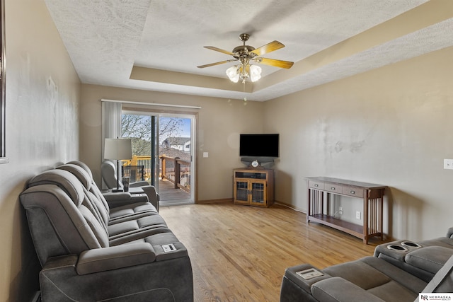 living room featuring wood finished floors, baseboards, ceiling fan, a textured ceiling, and a raised ceiling