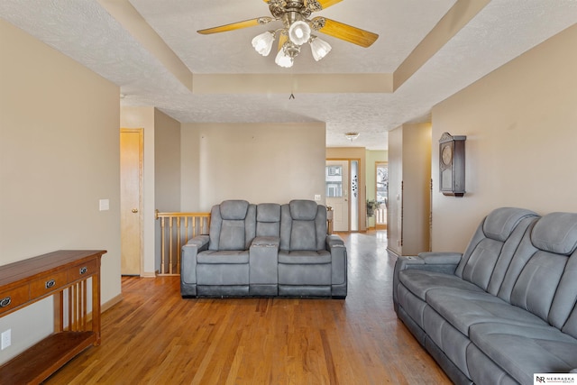 living area featuring light wood finished floors, a textured ceiling, a tray ceiling, and a ceiling fan