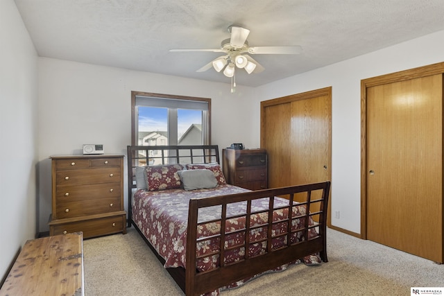 bedroom with carpet flooring, two closets, baseboards, and a ceiling fan