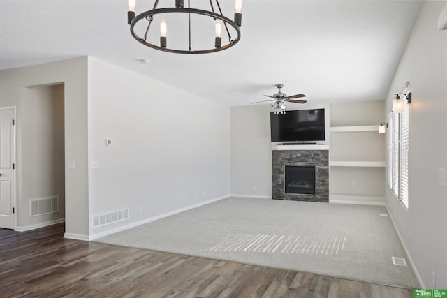 unfurnished living room featuring visible vents, ceiling fan with notable chandelier, a fireplace, and wood finished floors