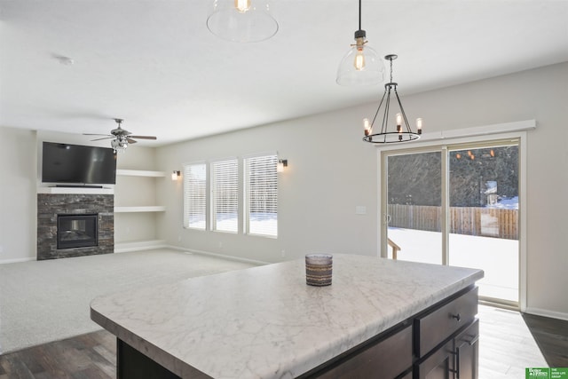 kitchen featuring pendant lighting, ceiling fan with notable chandelier, a glass covered fireplace, light countertops, and baseboards