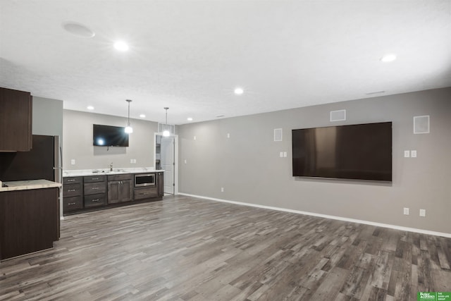 unfurnished living room featuring a sink, recessed lighting, baseboards, and wood finished floors