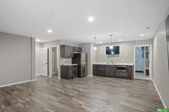 kitchen featuring stainless steel appliances, dark brown cabinets, wood finished floors, and light countertops