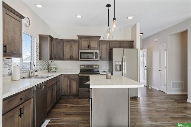 kitchen with visible vents, a sink, a kitchen island, dark wood-style floors, and appliances with stainless steel finishes