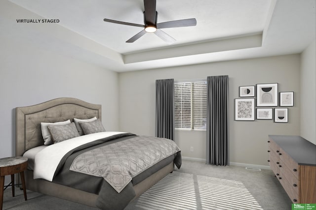 bedroom with a tray ceiling, baseboards, light carpet, and ceiling fan