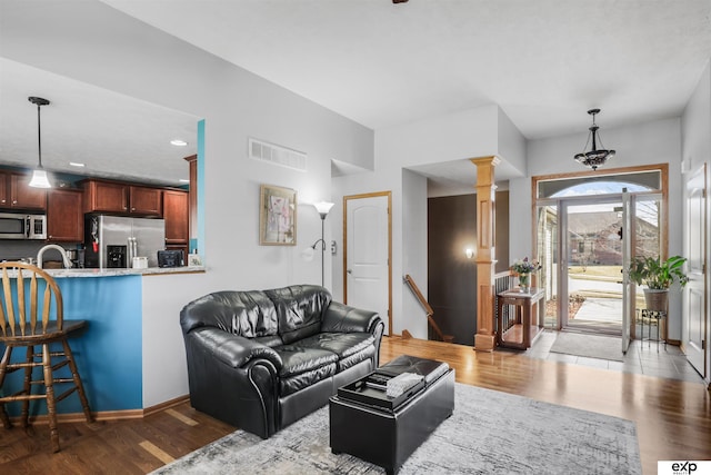 living area featuring visible vents, wood finished floors, baseboards, and decorative columns