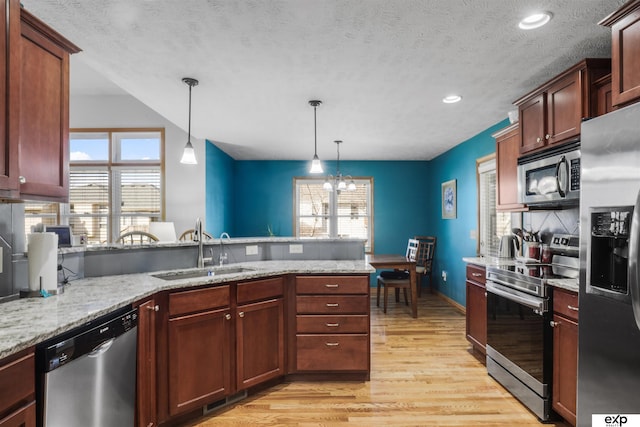 kitchen featuring a sink, stainless steel appliances, a peninsula, light wood finished floors, and hanging light fixtures