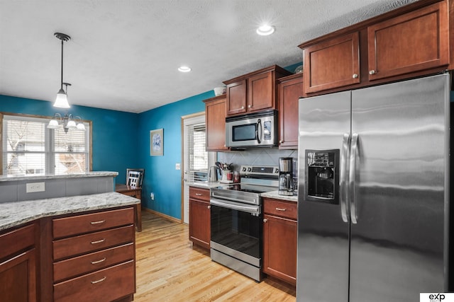 kitchen with light stone countertops, light wood-style flooring, hanging light fixtures, appliances with stainless steel finishes, and tasteful backsplash