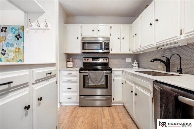 kitchen with light wood-style flooring, a sink, stainless steel appliances, light countertops, and tasteful backsplash