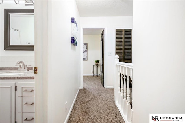 corridor with a sink, baseboards, carpet floors, and a textured ceiling