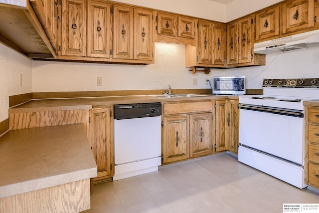 kitchen with white appliances, brown cabinetry, a sink, light countertops, and under cabinet range hood