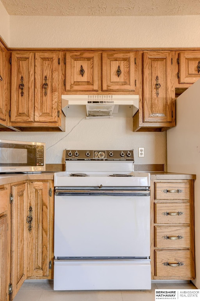 kitchen with white appliances, brown cabinets, under cabinet range hood, and a textured ceiling