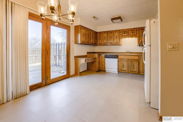 kitchen with white appliances, brown cabinetry, an inviting chandelier, a sink, and a textured ceiling