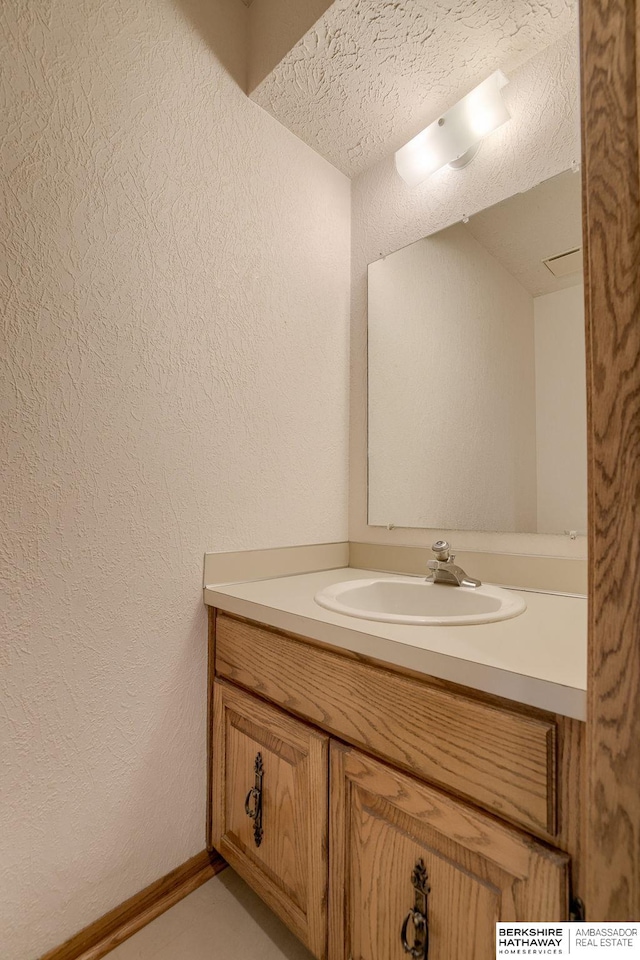 bathroom with baseboards, vanity, and a textured wall