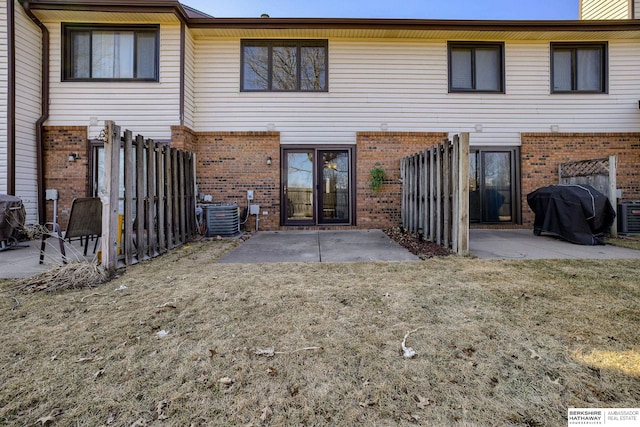 rear view of house with brick siding, fence, central AC unit, a lawn, and a patio