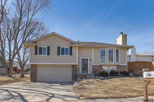 raised ranch featuring driveway, fence, a garage, brick siding, and a chimney