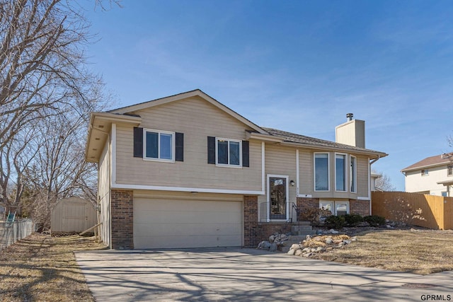 split foyer home with brick siding, a chimney, a garage, and fence