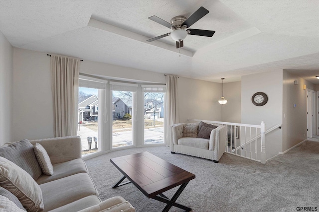 carpeted living area with a textured ceiling, a raised ceiling, baseboards, and ceiling fan