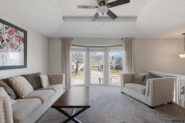 carpeted living area with a textured ceiling, a tray ceiling, and ceiling fan