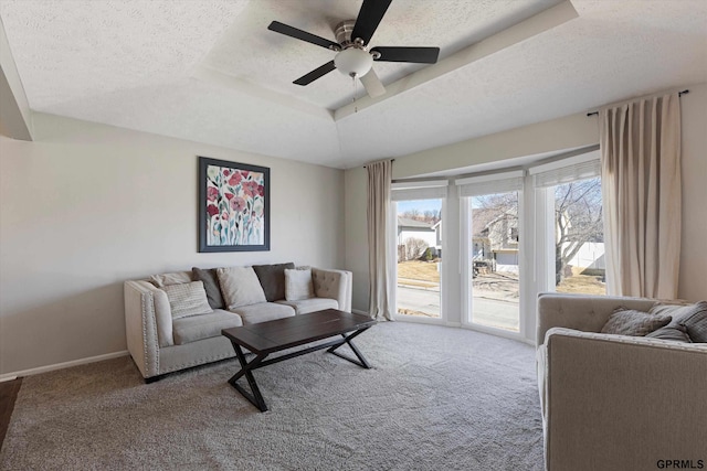 carpeted living area featuring ceiling fan, a tray ceiling, baseboards, and a textured ceiling