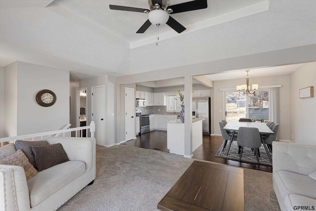 living room with a raised ceiling, ceiling fan with notable chandelier, baseboards, and dark carpet