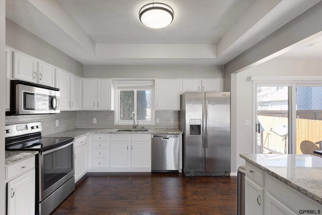 kitchen featuring a sink, light stone counters, stainless steel appliances, white cabinetry, and dark wood-style flooring