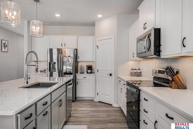 kitchen with wood finished floors, a sink, appliances with stainless steel finishes, white cabinetry, and decorative light fixtures