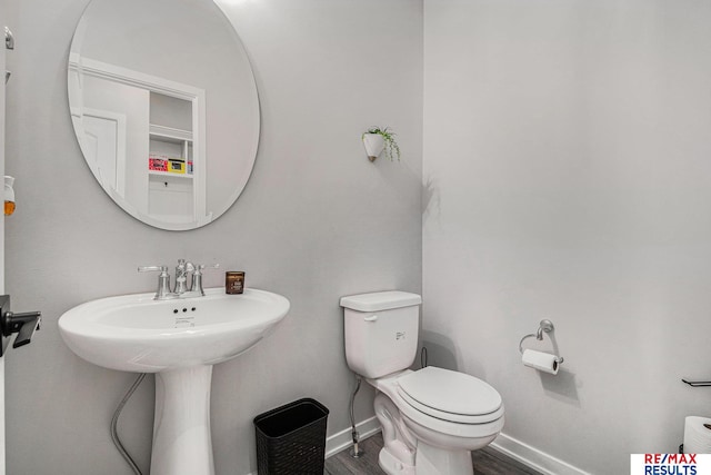 bathroom with toilet, wood finished floors, baseboards, and a sink