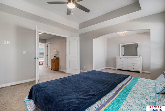 bedroom with baseboards, carpet flooring, arched walkways, a raised ceiling, and a ceiling fan