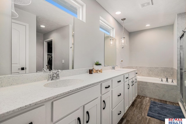 bathroom featuring wood finished floors, visible vents, a sink, a shower stall, and a garden tub