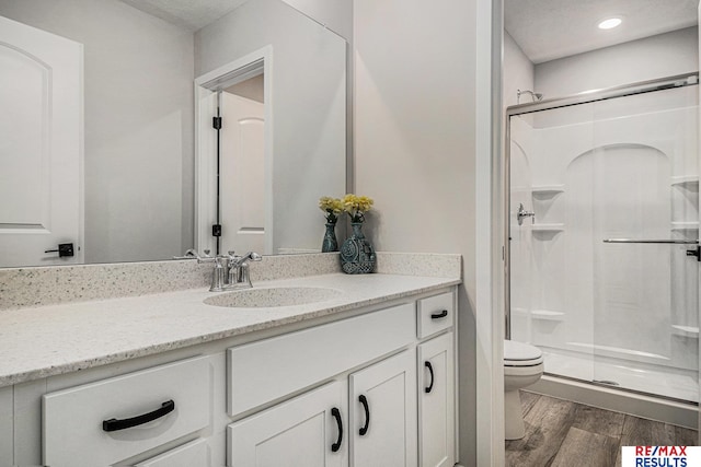 bathroom featuring vanity, wood finished floors, recessed lighting, a stall shower, and toilet