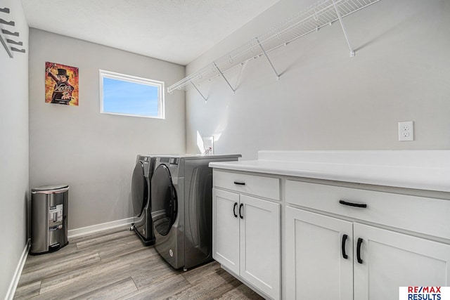 clothes washing area with cabinet space, washer and dryer, light wood-type flooring, and baseboards