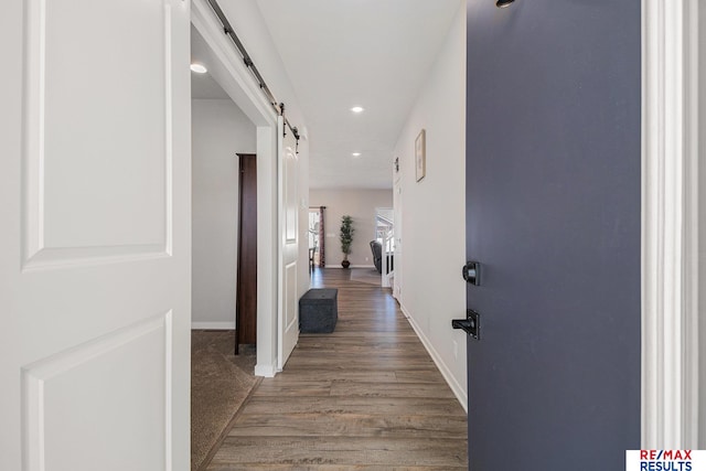 hallway featuring recessed lighting, baseboards, a barn door, and wood finished floors