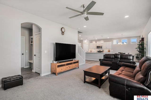 living area featuring baseboards, light carpet, recessed lighting, ceiling fan with notable chandelier, and arched walkways