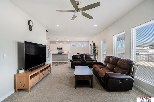 living area featuring light colored carpet, a ceiling fan, baseboards, and a wealth of natural light