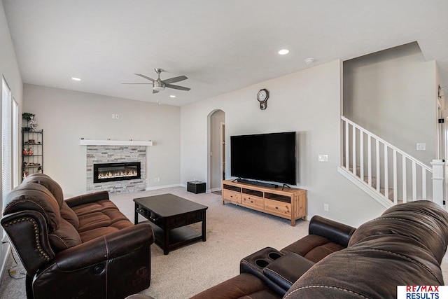 living room with recessed lighting, arched walkways, a stone fireplace, light colored carpet, and ceiling fan