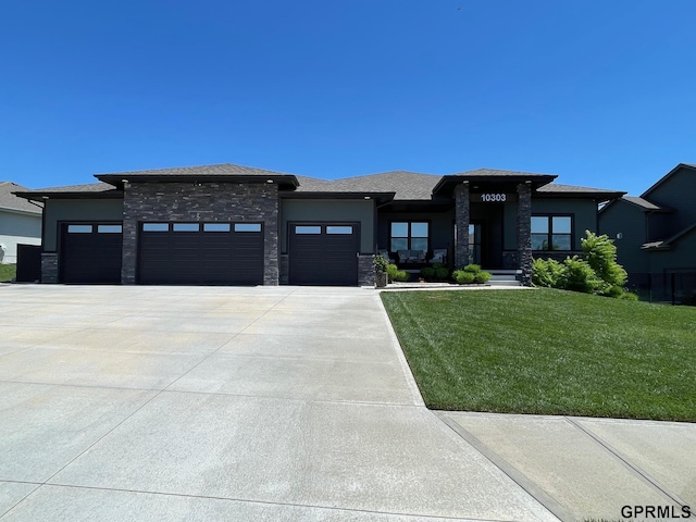 prairie-style home featuring a front yard, driveway, an attached garage, stucco siding, and stone siding