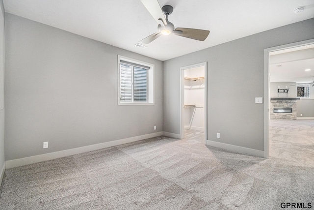 unfurnished bedroom with a spacious closet, baseboards, carpet floors, a glass covered fireplace, and a ceiling fan