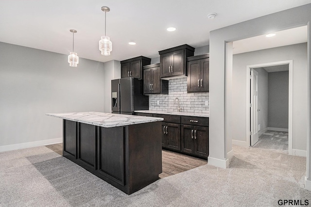 kitchen with a sink, decorative backsplash, hanging light fixtures, black refrigerator with ice dispenser, and a center island