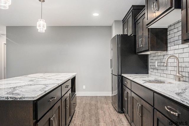 kitchen with light stone counters, light wood finished floors, a sink, pendant lighting, and tasteful backsplash