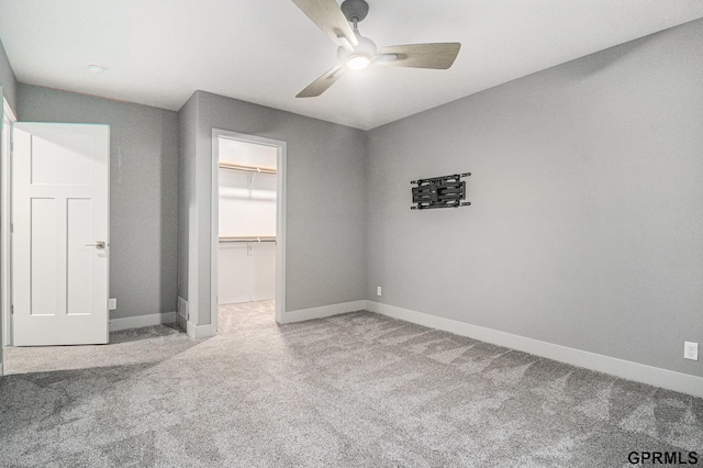 unfurnished bedroom with a walk in closet, a closet, baseboards, and carpet floors