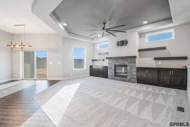 living room with baseboards, a raised ceiling, and ceiling fan with notable chandelier