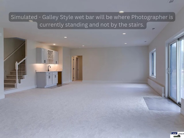 unfurnished living room featuring baseboards, recessed lighting, a sink, stairs, and light carpet