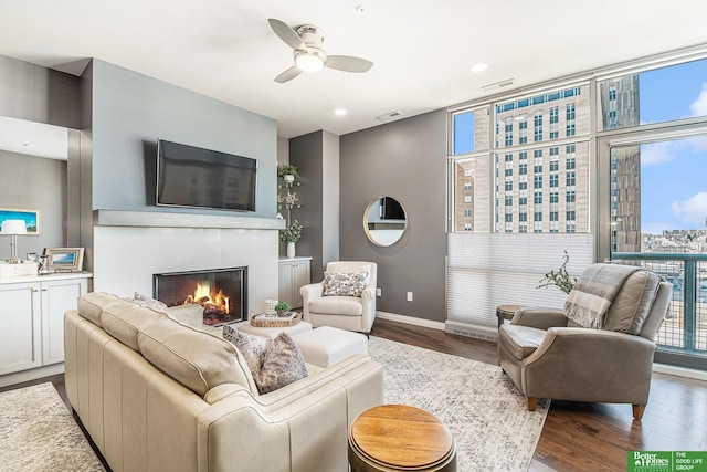 living area featuring a ceiling fan, visible vents, baseboards, dark wood finished floors, and a warm lit fireplace