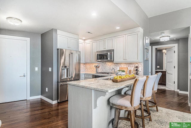 kitchen with a kitchen breakfast bar, tasteful backsplash, dark wood-style floors, appliances with stainless steel finishes, and light stone countertops