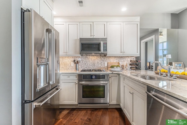 kitchen with visible vents, a sink, appliances with stainless steel finishes, light stone countertops, and dark wood-style flooring