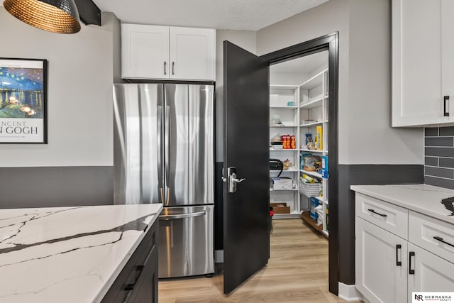 10230 Weir St, Ralston, NE 68127 - kitchen featuring light stone counters, light wood-style flooring, white cabinets, and freestanding refrigerator